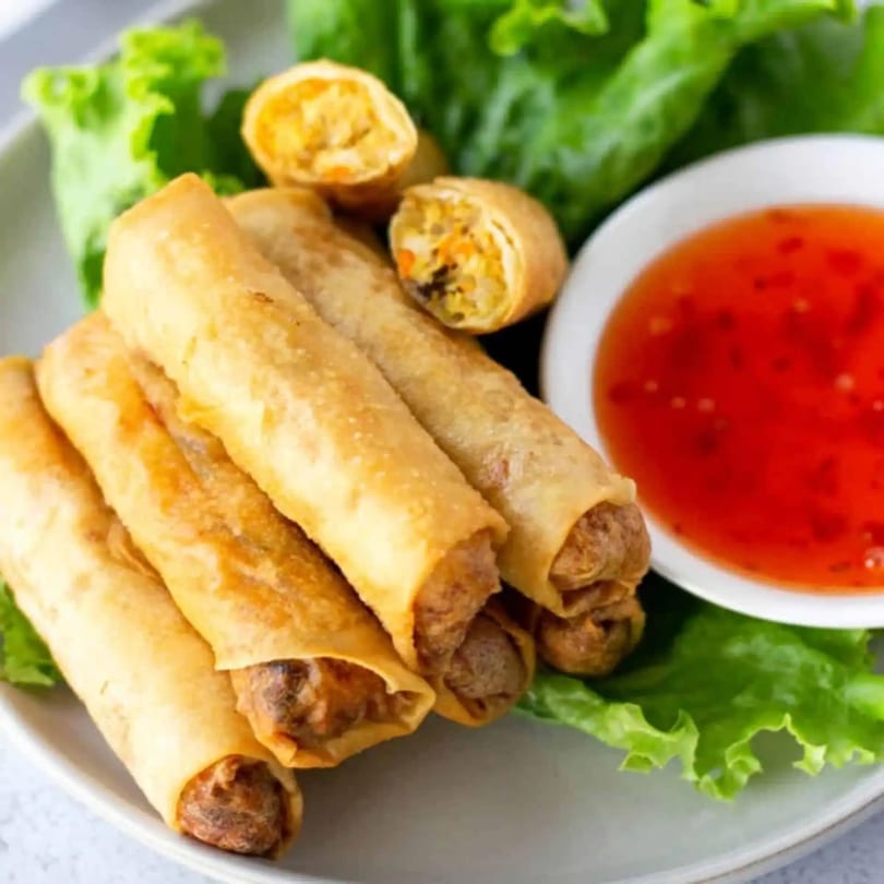 Crispy golden spring rolls with a sweet chili dipping sauce and fresh lettuce on a plate.