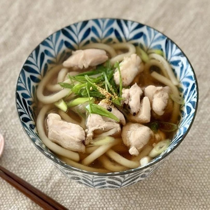 Chicken Udon soup in a blue and white patterned bowl, garnished with green onions and spices.