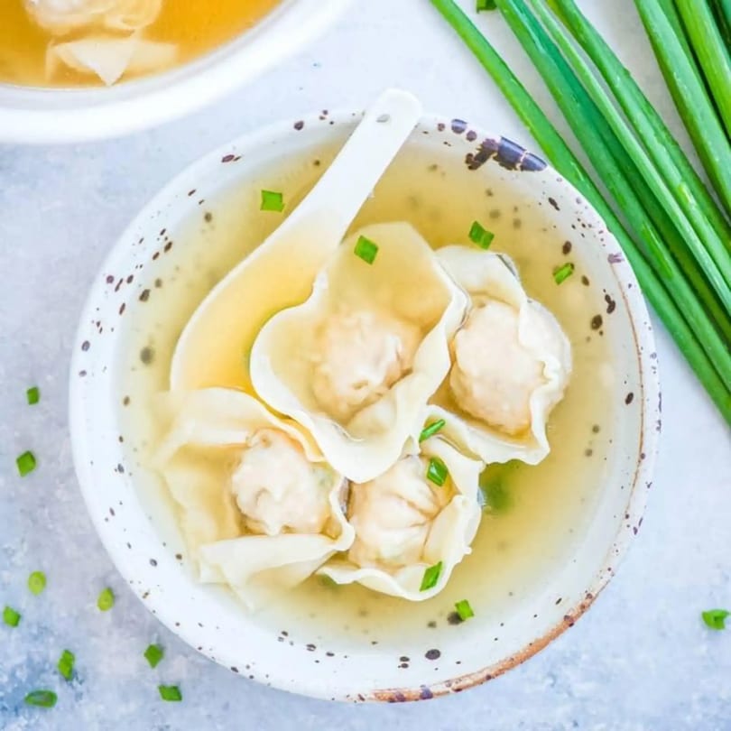 A bowl of Linsway Grill & Teriyaki wonton soup with a spoon, garnished with green onions.